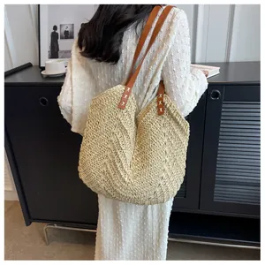 Détail d'un cabas en paille beige avec anses en cuir marron et coutures en croix blanches