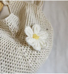 Detail of hollow woven beach tote featuring a 3D white knitted flower with yellow center