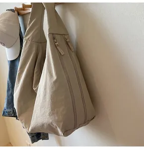 Detail of beige nylon tote bag with dual zipper design hanging on wooden coat rack