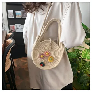 Détail d'un sac rond en paille tressée orné de fleurs 3D et d'une bandoulière