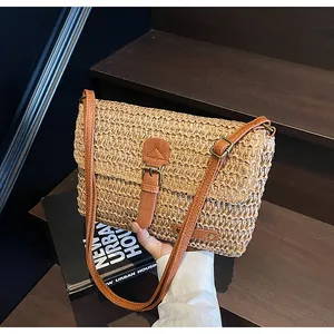 Detail van handgeweven strooien strandtas met bruine leren riem en retro metalen gespsluiting