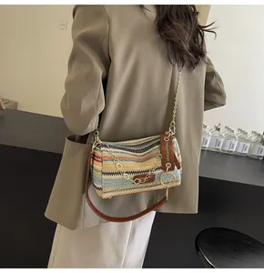 Detail of a rainbow woven cylinder bag with gold chain and brown leather strap on a model