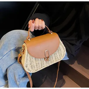 Detail of woven straw handbag with brown leather flap and golden metal clasp closure