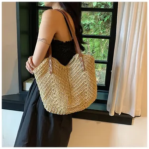 Détail du sac cabas en paille tressée avec bandoulières en cuir marron sur un modèle