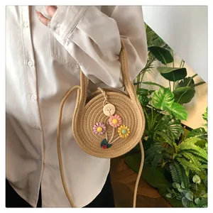 Détail du sac rond en paille avec fleurs tricotées et coccinelle sur chemise blanche