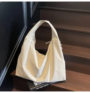 Detail of a large beige crescent tote bag placed on a wooden step with a book