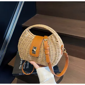 Detailansicht der gewebten Strohtasche mit braunem Lederriemen und Metall-Drehverschluss