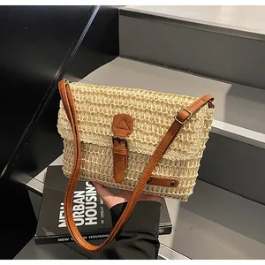 Detail van beige geweven strooien tas met bruine kunstleren riem en metalen gespen