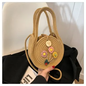 Détail d'un sac rond en paille avec des fleurs colorées et un petit pendentif