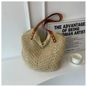 Détail du sac cabas en paille beige avec anses en cuir marron et coutures en croix blanches