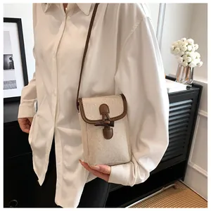 Close-up of beige canvas crossbody phone bag with brown leather trim and horn buckle