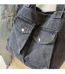 Détail d'un sac cabas en jean noir avec texture délavée et deux poches à boucle argent