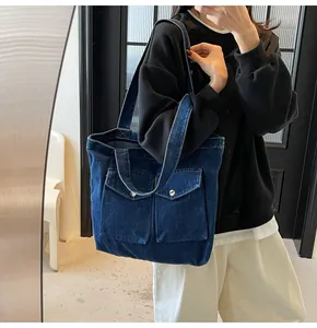Détail d'un sac cabas en jean bleu avec deux poches frontales et des boutons argentés