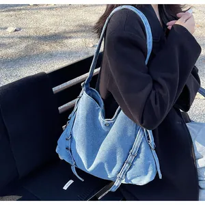 Detail of blue denim shoulder bag showing texture and metal rings in natural sunlight