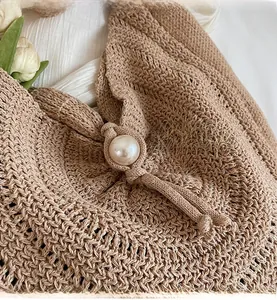 Detail of hand-woven straw tote bag with a large white pearl closure on silk background