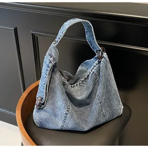 Close-up of denim shoulder bag with knotted leather strap and silver rivet details