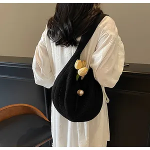Detail of black knit hobo bag featuring large pearl button and yellow tulip floral accent