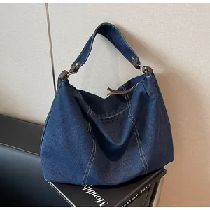 Detail of blue denim hobo bag with white stitching and dark brown leather accents