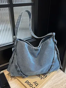 Large light blue denim hobo shoulder bag with metal rings on a stone surface