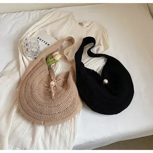 Detail of knit shoulder bags with pearl closures in beige and black displayed with tulips