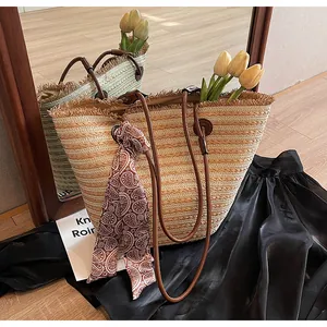 Détail du sac cabas en paille tressée avec lanières en cuir brun et foulard en soie