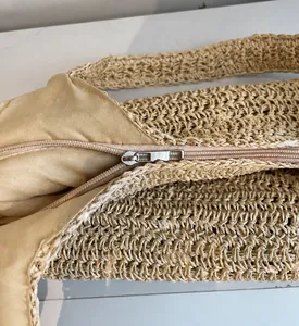 Detailed macro view of the smooth metal zipper and woven texture on a beige straw bag