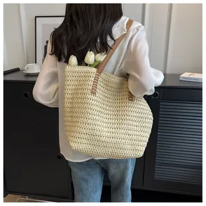 Détail du tissage en paille et de la bandoulière en cuir marron sur un sac crème