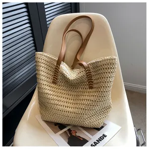 Gros plan sur un sac cabas en paille beige avec anses en cuir brun et surpiqûres en X