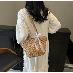 Vue détaillée du sac à bandoulière en paille tressée avec un grand nœud en dentelle blanche