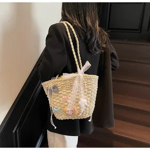 Détail du sac en paille tissée avec nœud en dentelle blanche et rubans en soie