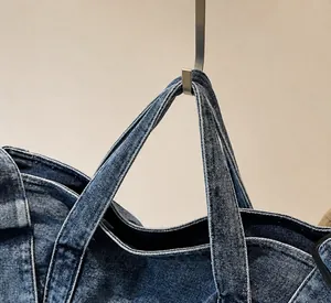 Detailed close-up of dark blue denim tote bag reinforced handles and stitching quality