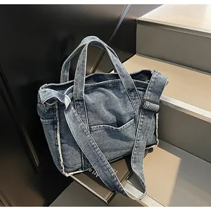 Close-up of blue denim tote bag detail showing frayed edges and adjustable shoulder strap