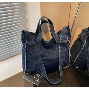 Detail of dark blue denim tote bag showing raw edge finish and adjustable shoulder strap