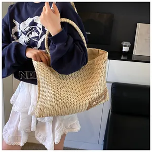 Dettaglio di una borsa tote in paglia intrecciata beige con scritta ALOHA e manici