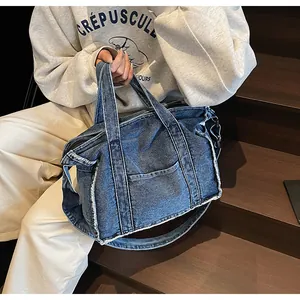 Deep blue denim tote bag with frayed edges and front pocket shown on a model