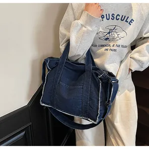 Detail of dark blue denim tote bag showing frayed edges and adjustable shoulder strap