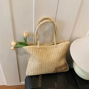 Dettaglio della trama della borsa tote in paglia con toppa in pelle su sfondo di legno bianco
