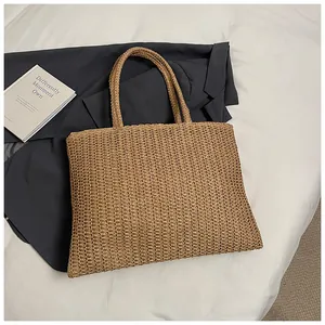 Vista piatta di una borsa tote in paglia intrecciata con doppi manici e fibre tessute
