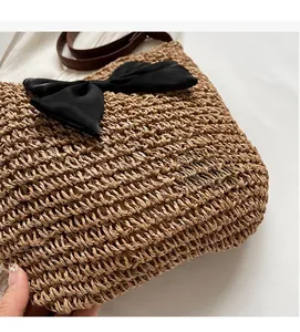 Detail der gewebten Strohtasche mit schwarzer Satinschleife und braunem Lederriemen