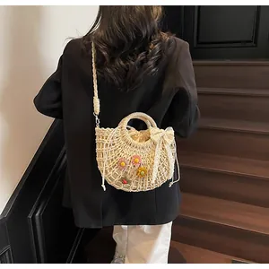 Detailed close-up of straw woven crossbody bag with pink flowers and lace bow