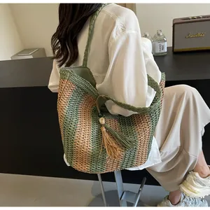 Detail of striped straw tote bag featuring green tassels and woven shoulder straps