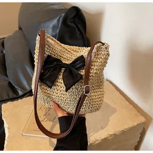 Detail der gewebten Strohtasche mit schwarzer Schleife und braunem Lederriemen