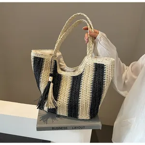 Detailed close-up of woven straw tote bag with black stripes and decorative tassel charm