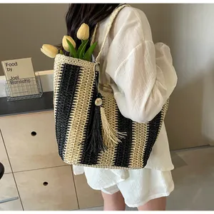 Detail view of woven straw tote bag with black stripes and decorative long fringe tassels