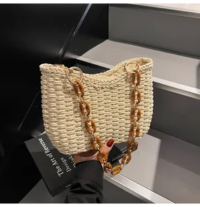 Detail of off-white straw bag featuring amber resin chain and golden hardware
