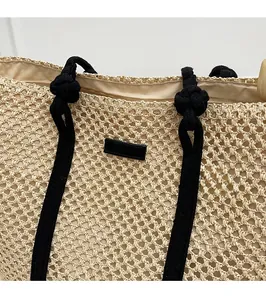 Détail du sac cabas en paille tissée avec anses en corde noire nouée et écusson en cuir