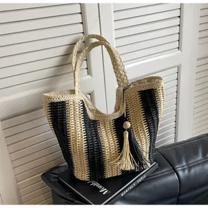 Detail of woven straw tote bag featuring vertical stripes, dual handles and tassel charm