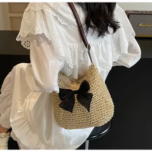 Detail der gewebten Strohtasche mit großer schwarzer Schleife und braunem Lederriemen