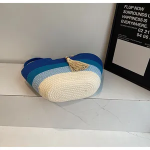 Détail du sac de plage tissé bicolore avec pompon posé sur des marches en marbre