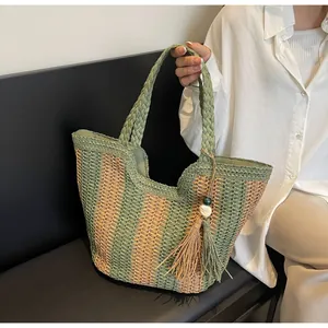 Detail of green and natural straw tote bag featuring tassel charm and woven texture